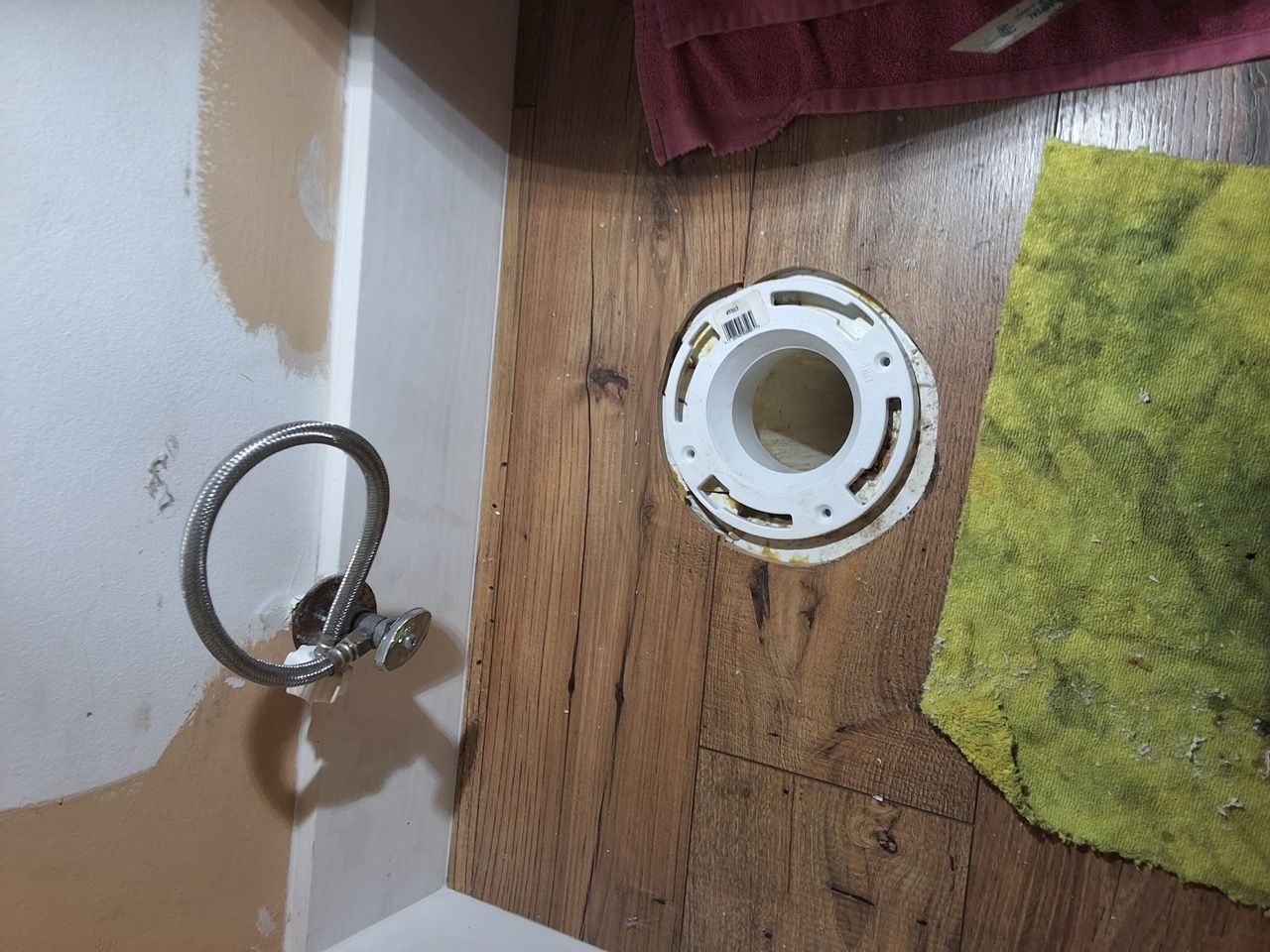 Bathroom floor with a detached toilet flange ring next to a green towel and wall corner