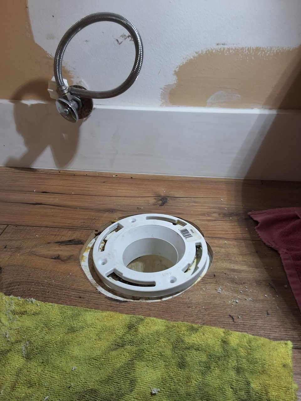 Bathroom wall with exposed plumbing and a white toilet flange on the floor near a baseboard.