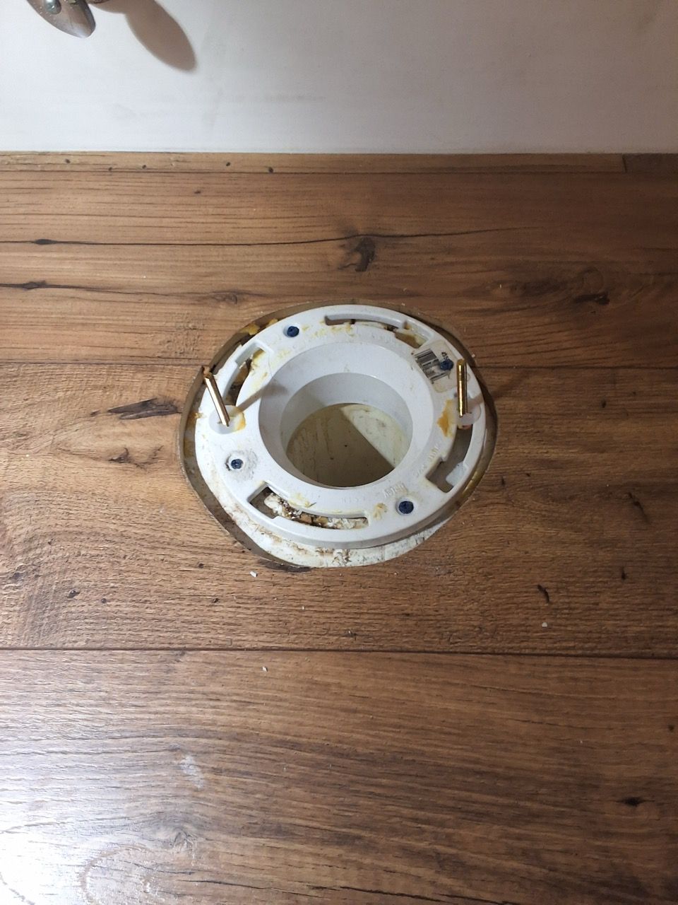 White plastic floor flange with rust stains on a wooden surface