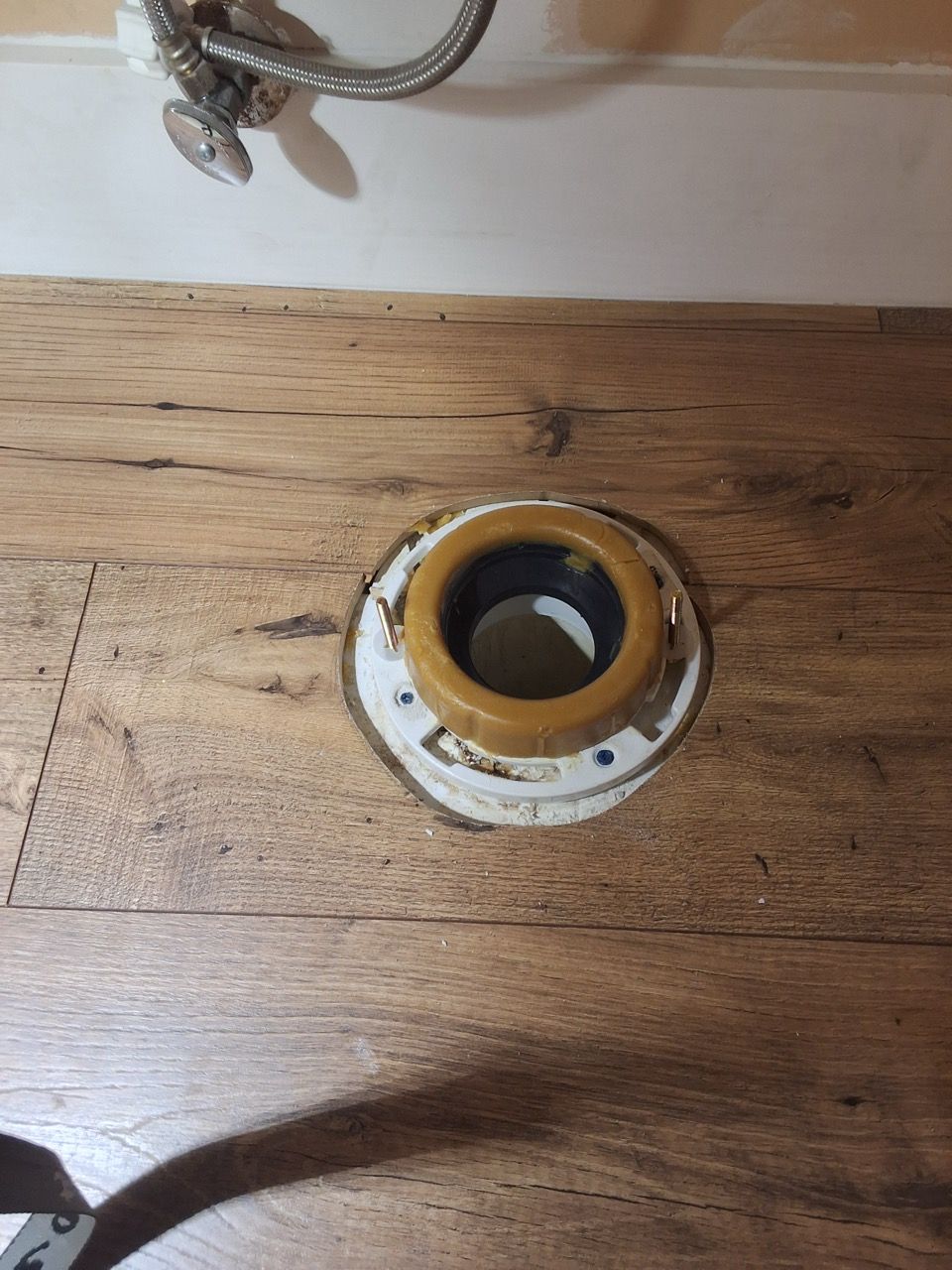 Brass toilet flange opening on a wooden floor with a rope visible nearby
