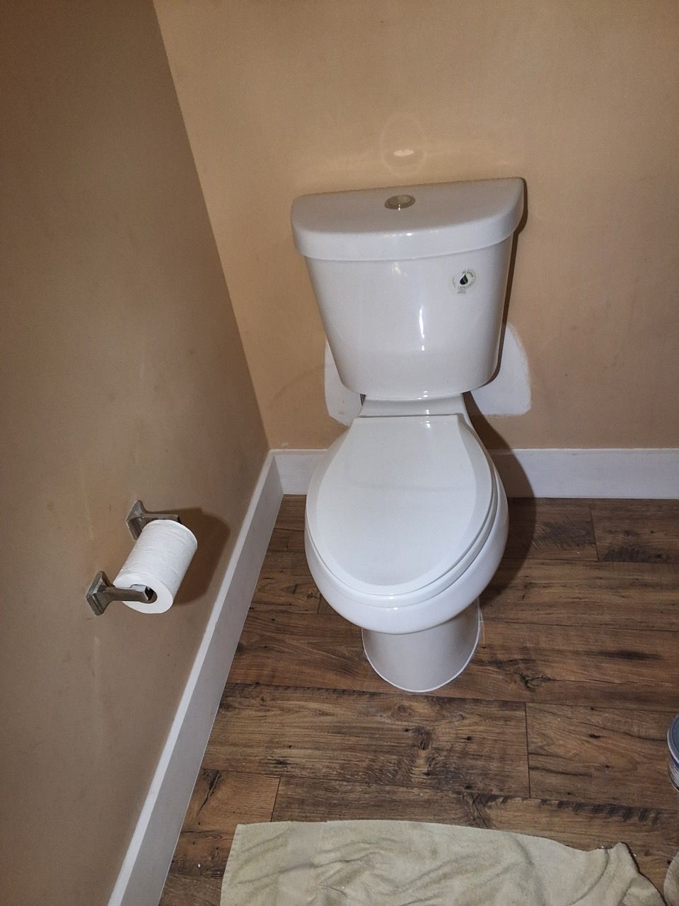 Small bathroom with a white toilet, toilet paper holder, beige walls, and wood-look flooring.