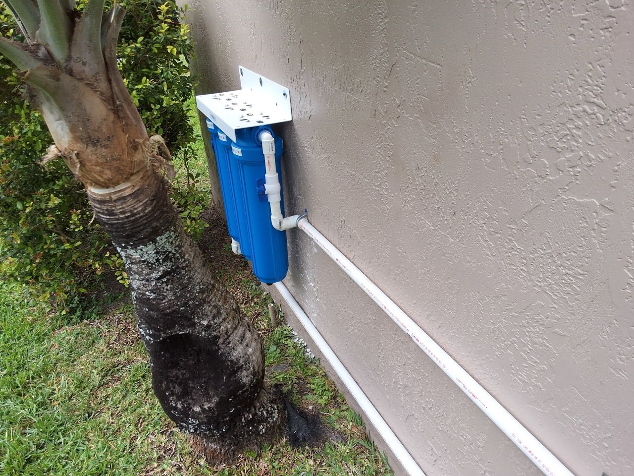 Blue utility box mounted on a stucco wall beside a tree and white conduit pipes