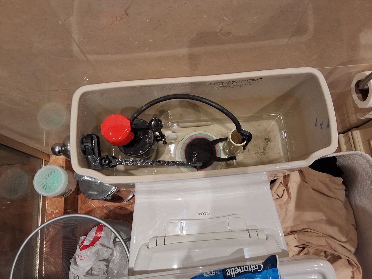Open toilet tank with float valve and a red cap inside the bathroom.