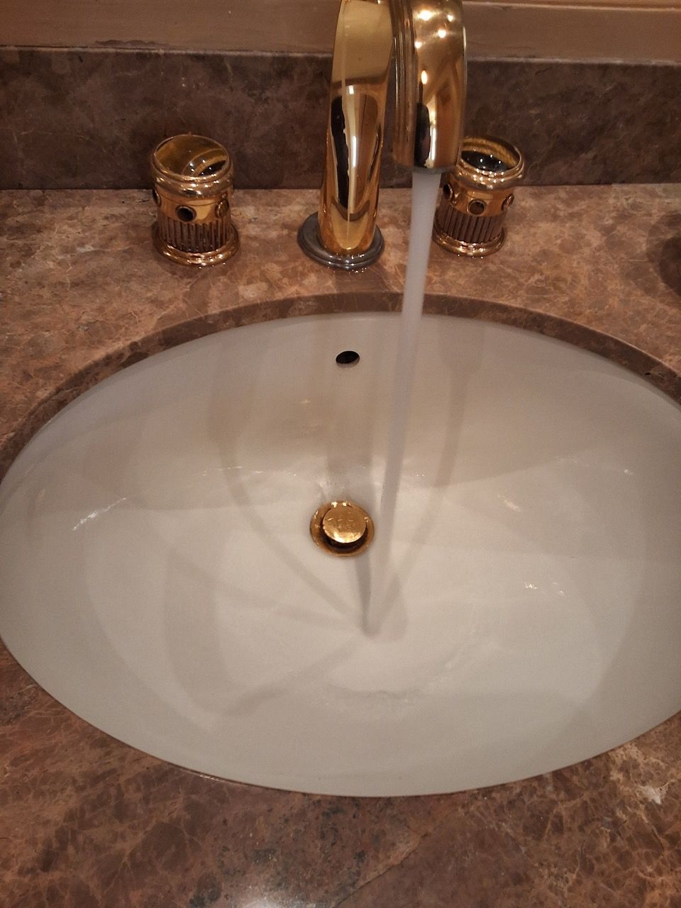Bathroom sink with running faucet and gold fixtures on a brown countertop.