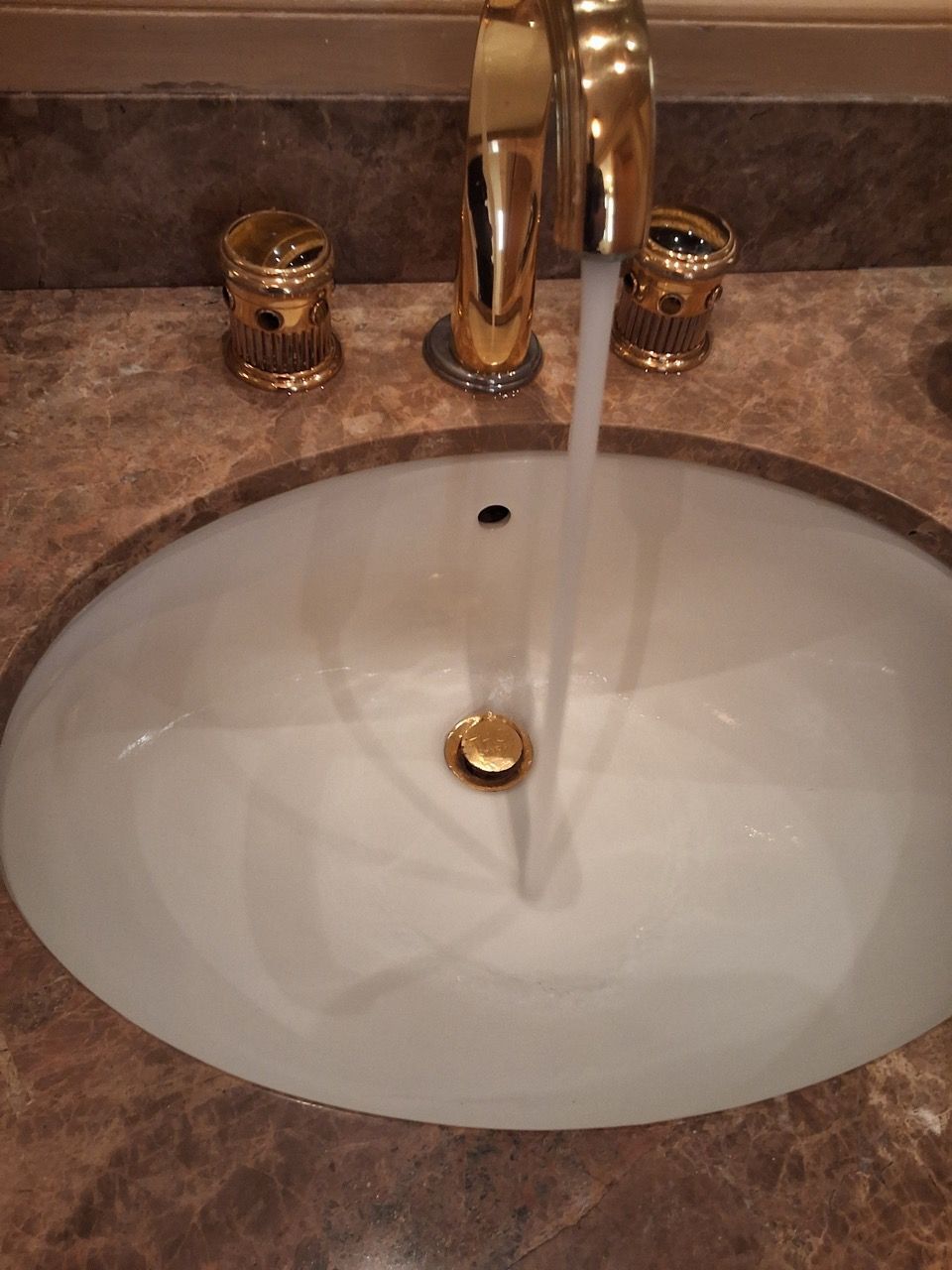 Bathroom sink with running water, chrome faucet, and brown countertop.