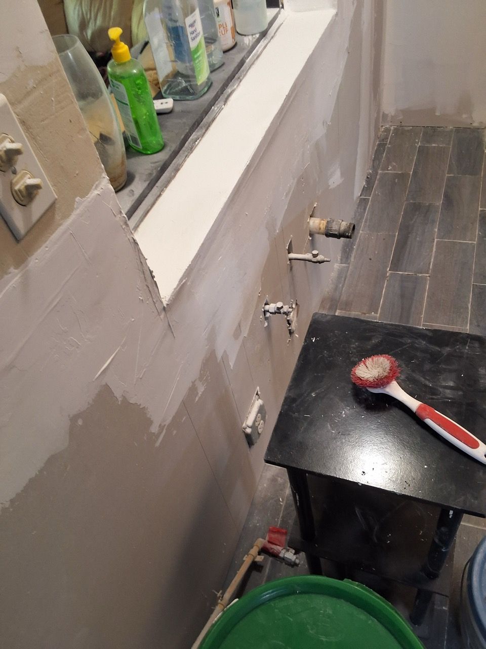 Bathroom wall with fresh patching, a sink ledge, and a red-and-white tool on a black stool