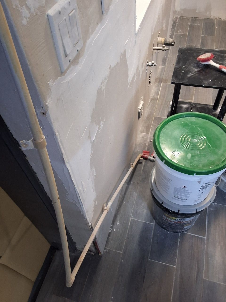 Paint bucket and wall trim in a narrow hallway with tools and unfinished painting work.