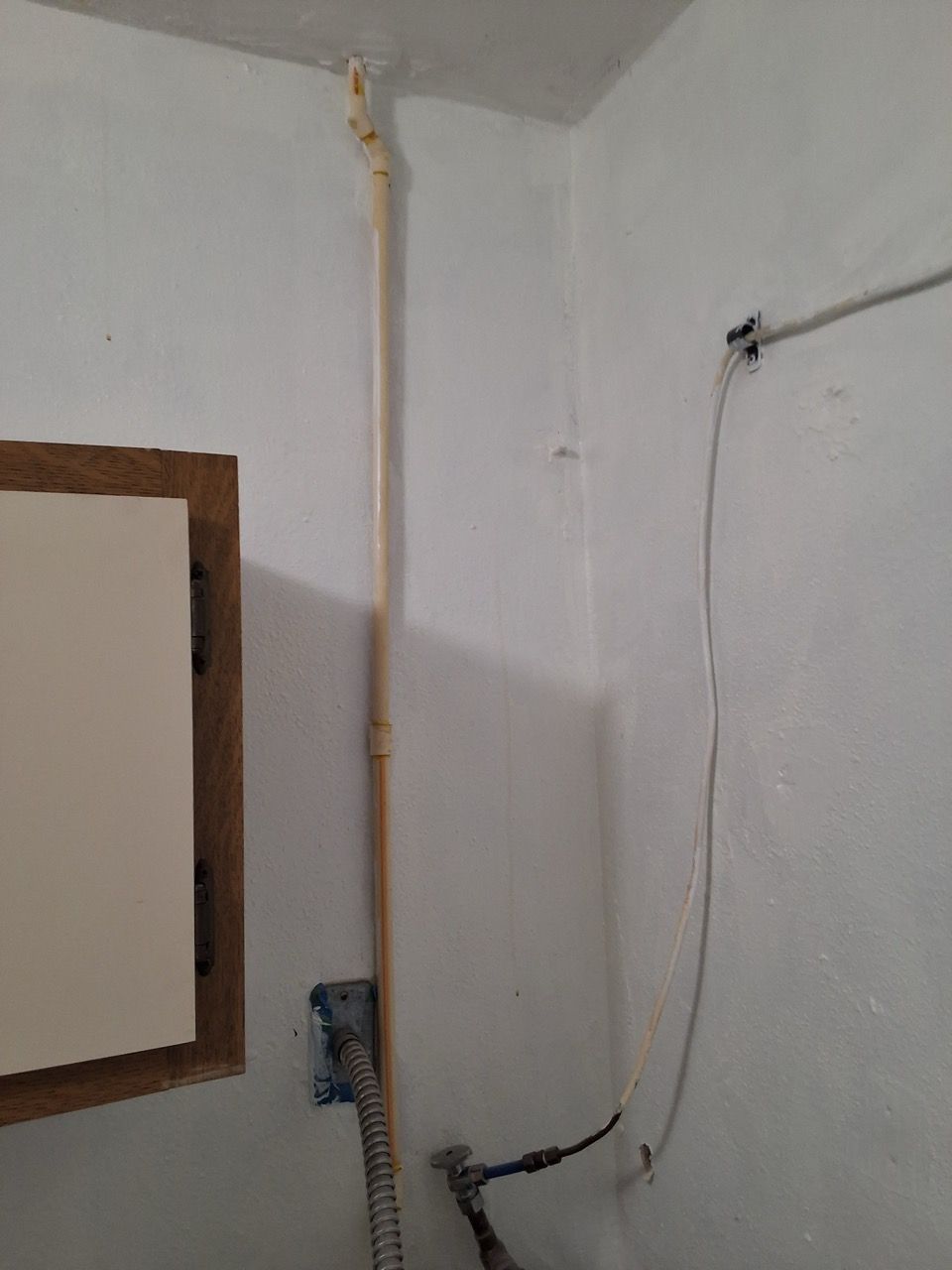 White interior wall corner with exposed wiring, a vertical conduit, and a small mounted box.