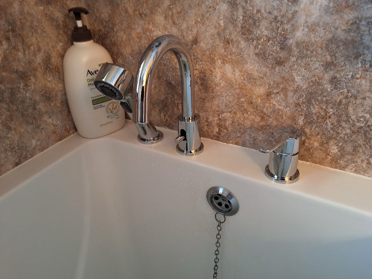 Bathtub faucet and soap dispenser beside a showerhead on a white tub edge