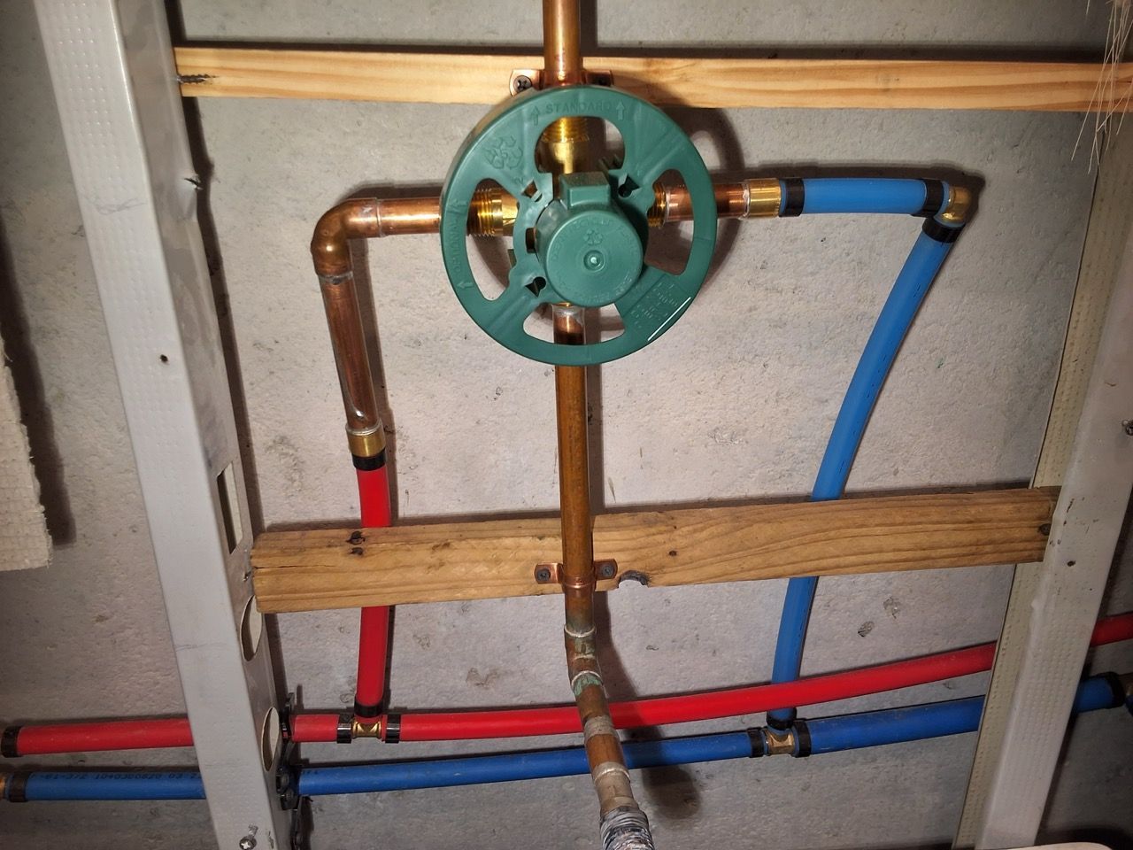 Green valve on copper pipes inside a wall frame with red and blue plumbing lines