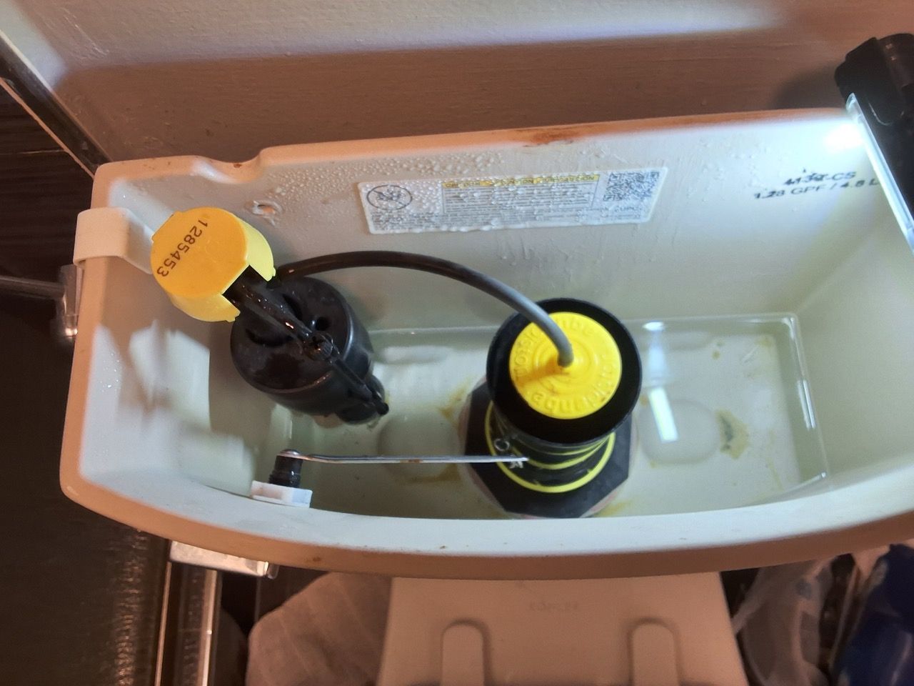 Inside a toilet tank, two black-and-yellow valve parts connected by a tube.
