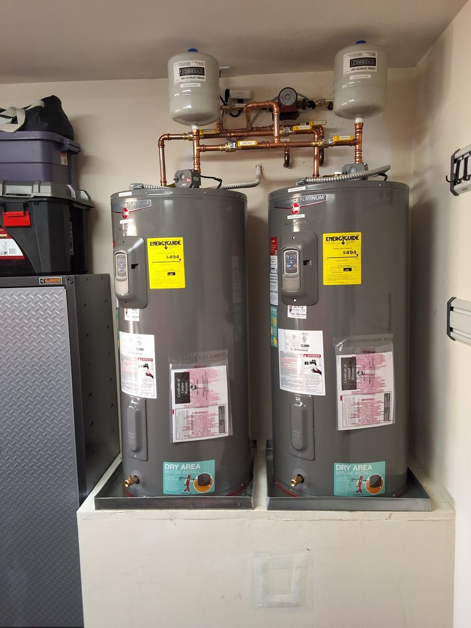 Two large gray water heaters with copper piping in a utility room