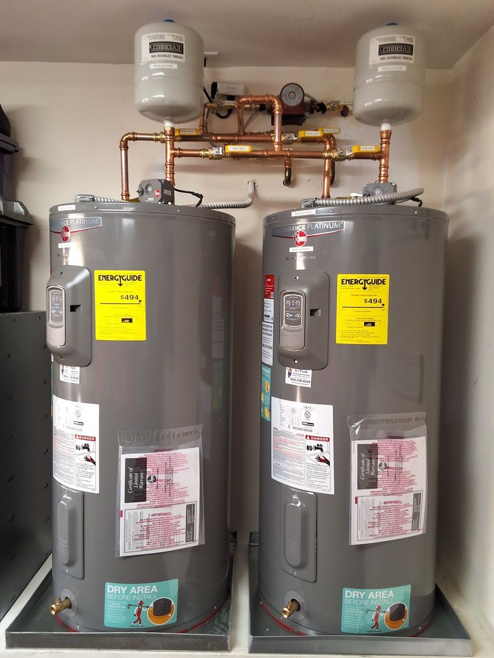 Two gray water heaters with copper pipes and expansion tanks in a utility closet