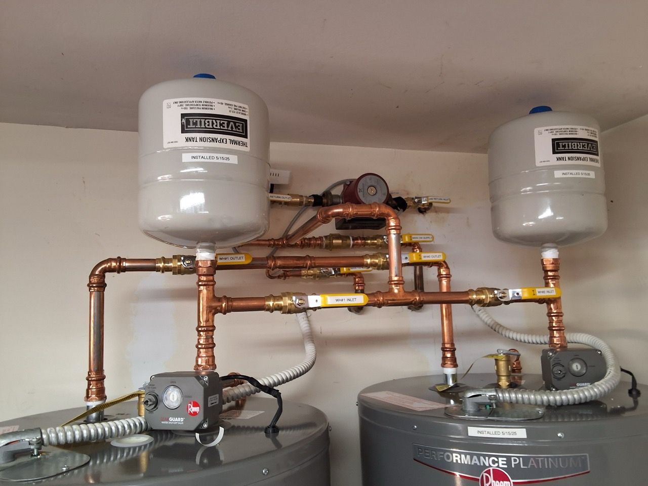 Plumbing setup with copper pipes, two white tanks, and water filtration equipment mounted on a wall and floor.
