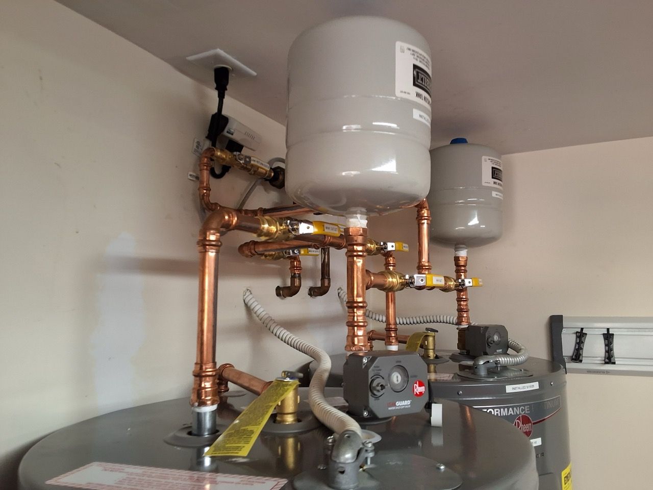 Copper plumbing and two white tanks above a water heater in a utility room
