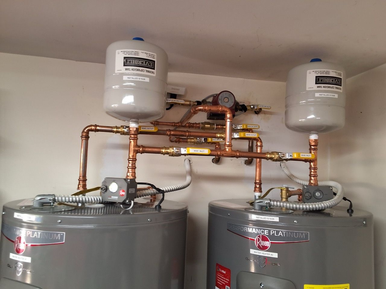 Two water heaters with copper piping and expansion tanks in a utility room