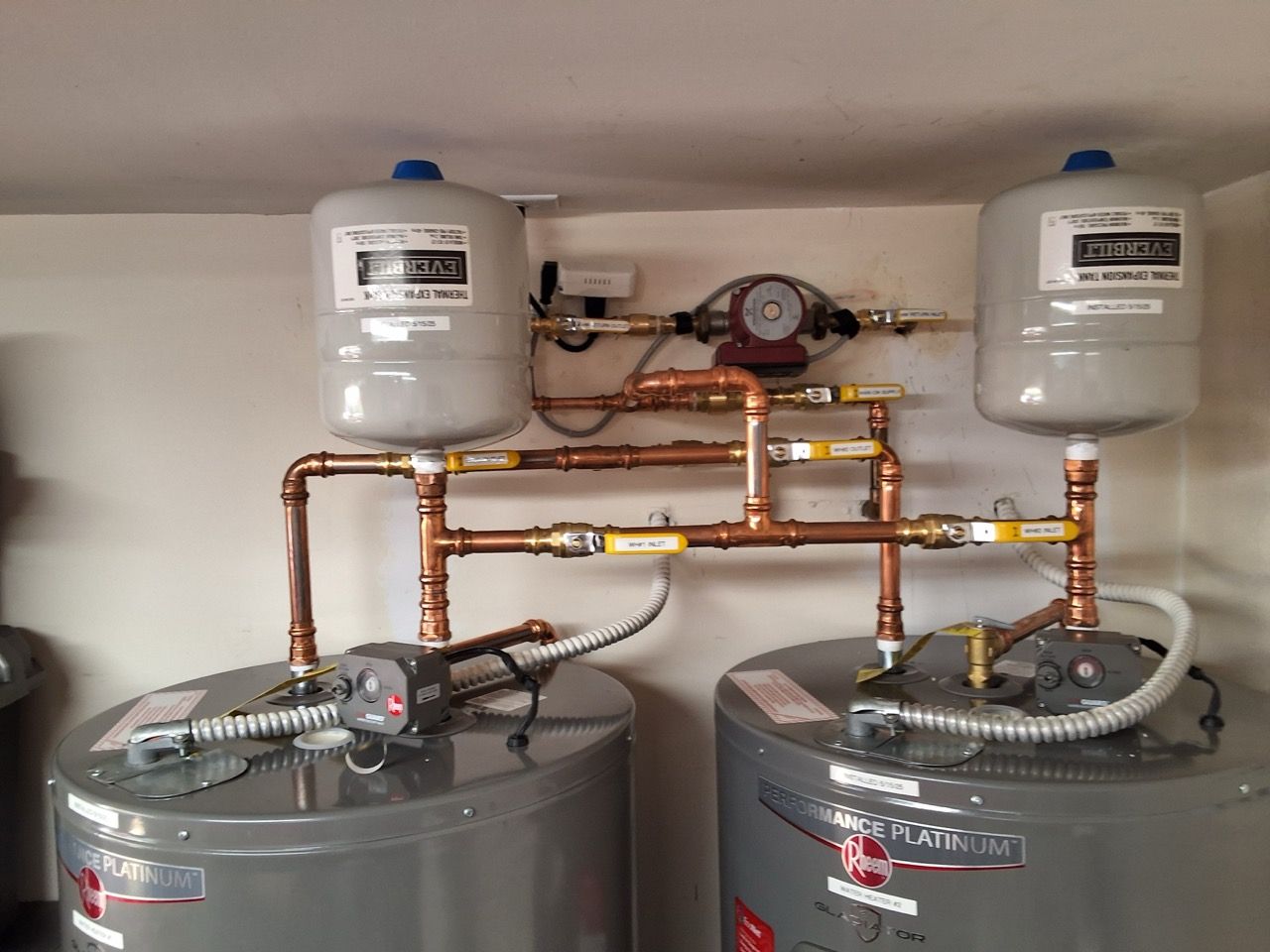 Boiler room with two water heaters, copper piping, and two large tanks below.