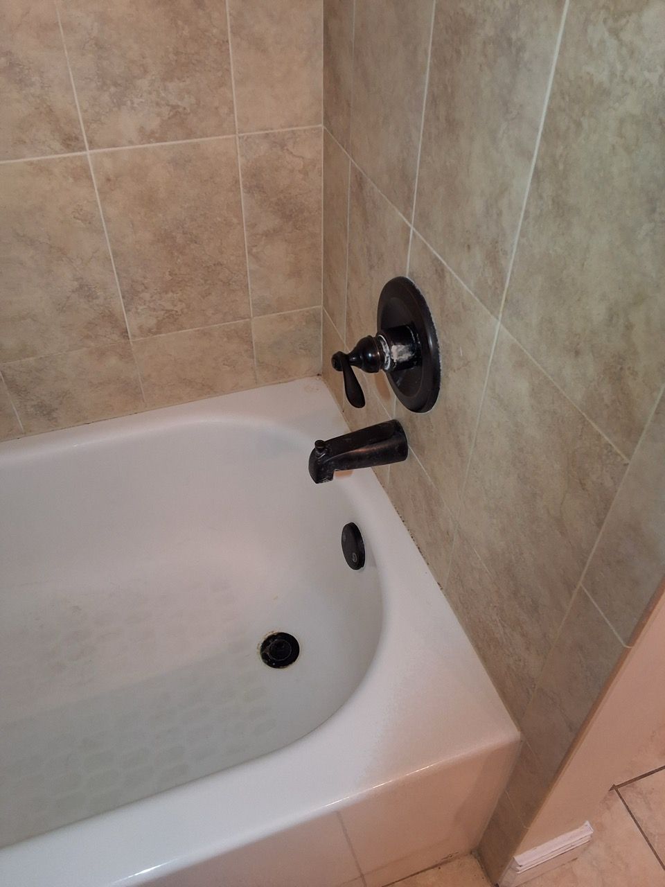 White bathtub with black faucet and beige tile walls in a bathroom
