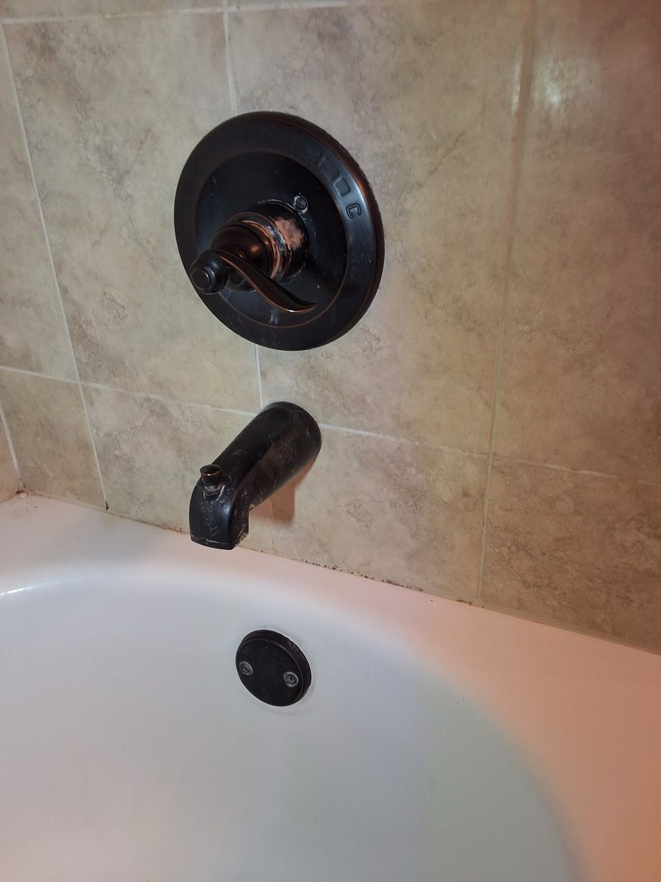 Shower faucet and tub drain with beige tile wall behind it