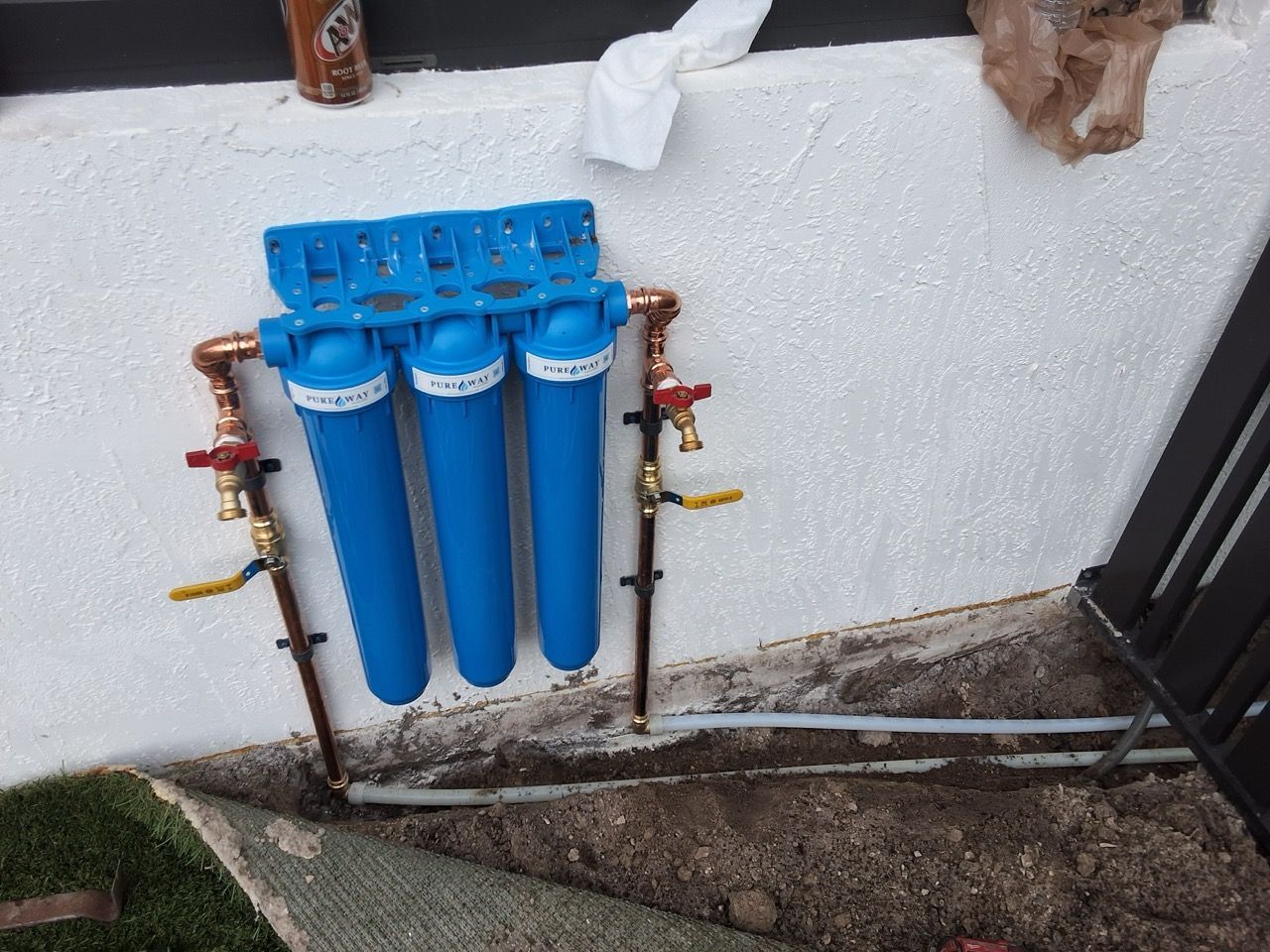 Blue water filter system mounted on an exterior wall with copper pipes and valves