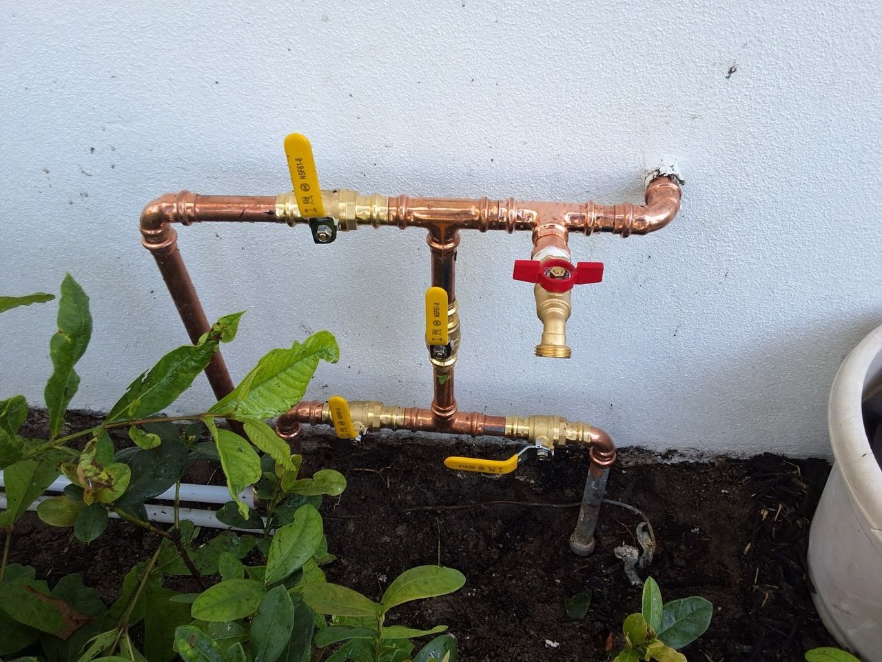 Copper pipe irrigation manifold with yellow and red valves above garden plants.