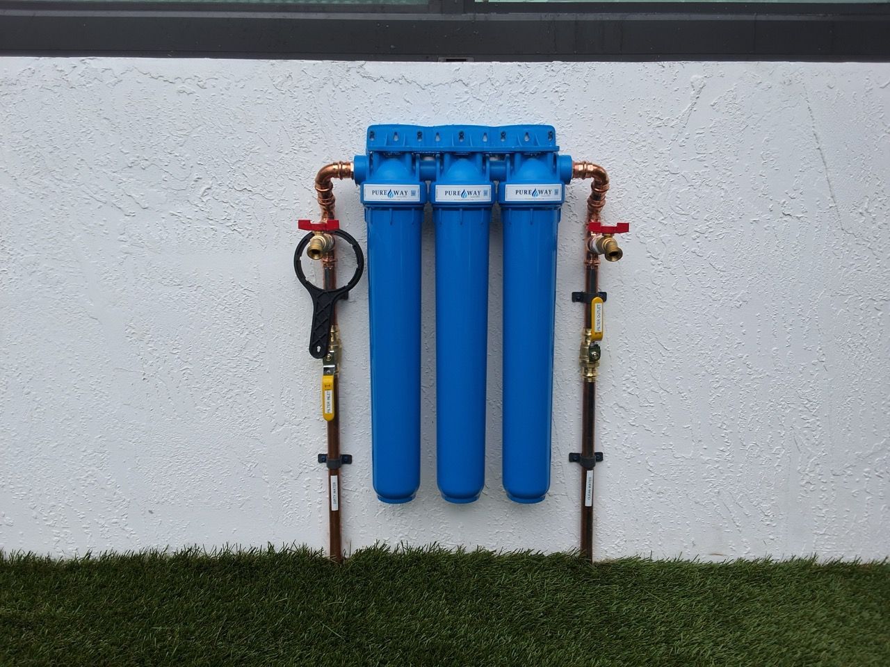 Blue water filtration system mounted on an exterior wall above grass
