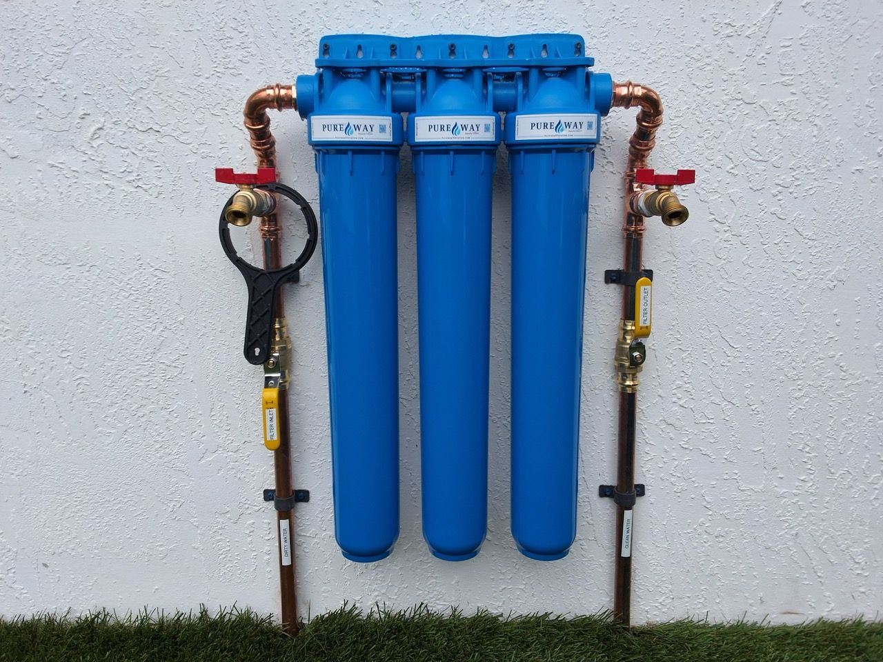 Three blue water filters mounted on a wall with copper pipes and valves