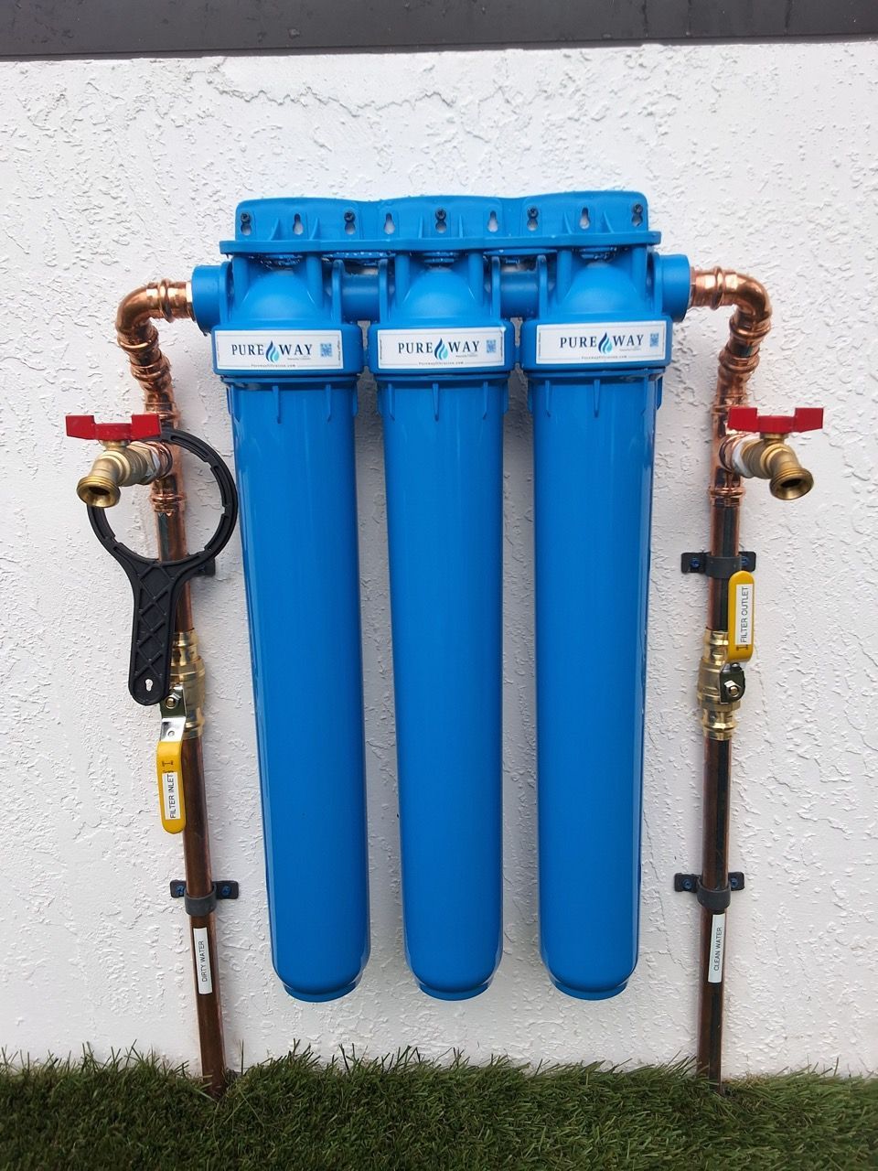 Three blue water filters mounted on a wall with copper pipes and red-handled shutoff valves