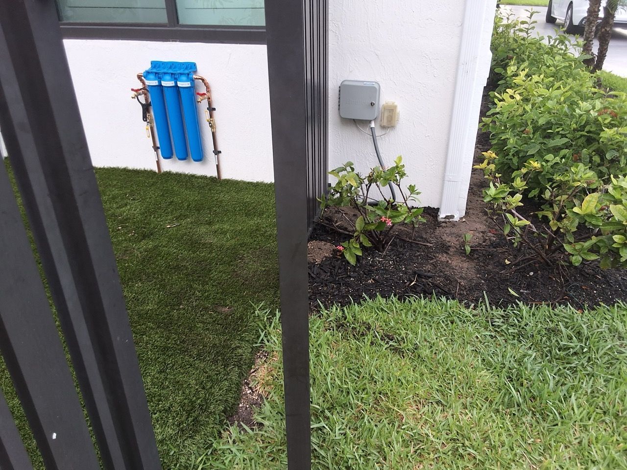 Apartment walkway with black railings, grass, and a blue utility box on the wall near shrubs.