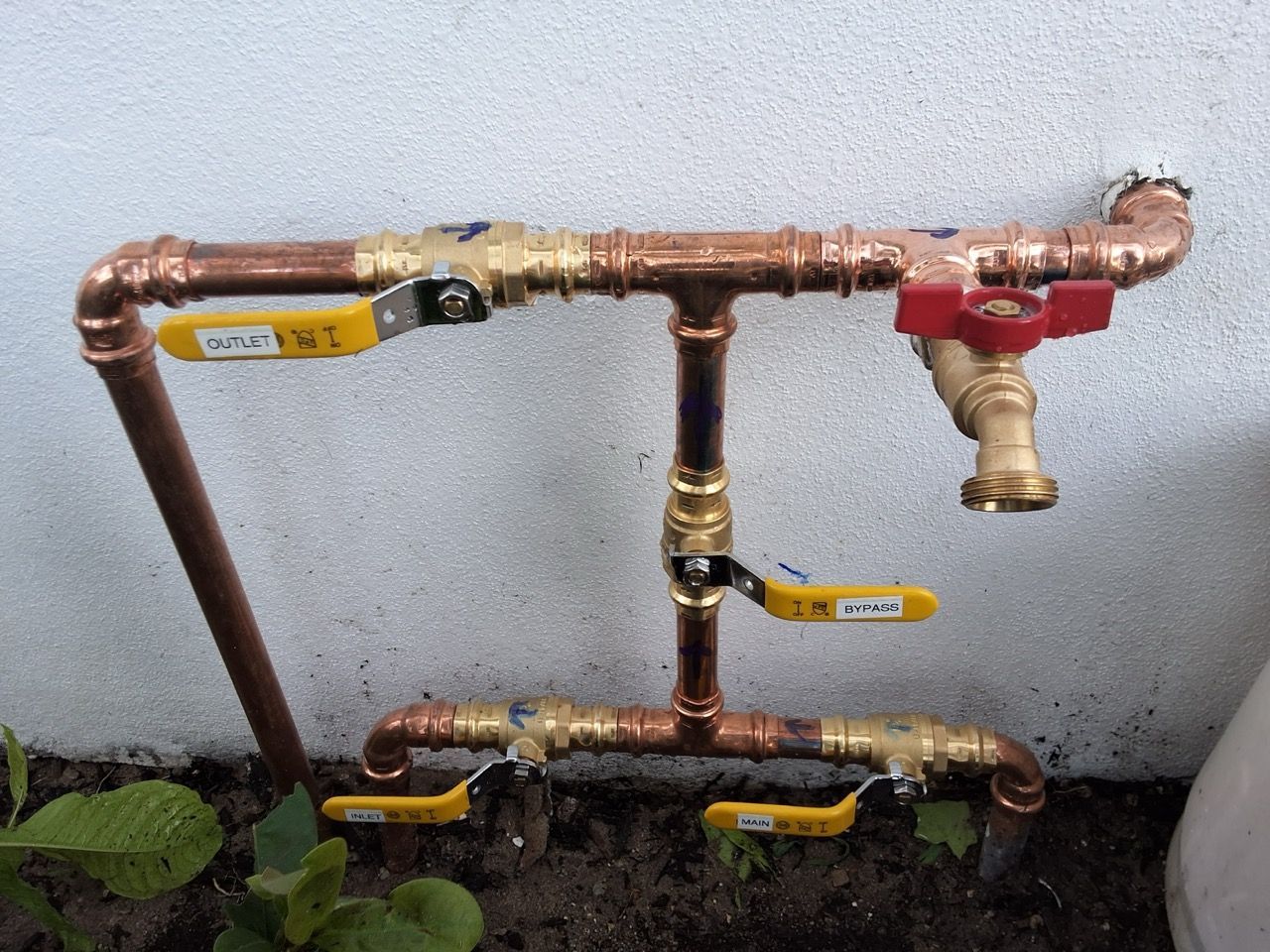 Copper gas pipes with yellow and red shutoff valves mounted on a wall above plants
