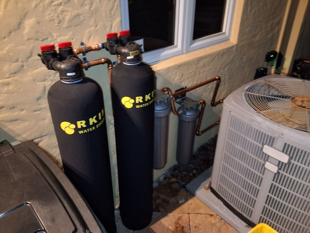 Black water treatment tanks beside an outdoor HVAC unit and window on a patio