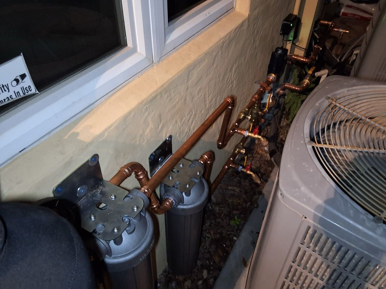 Indoor HVAC piping and valves beside a window and a large fan unit.