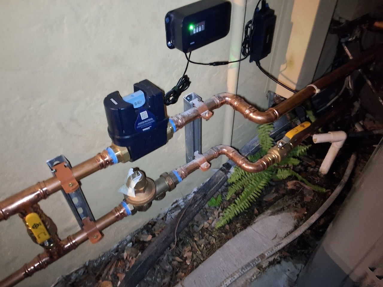 Water meter and copper pipes mounted along a wall in a narrow utility space