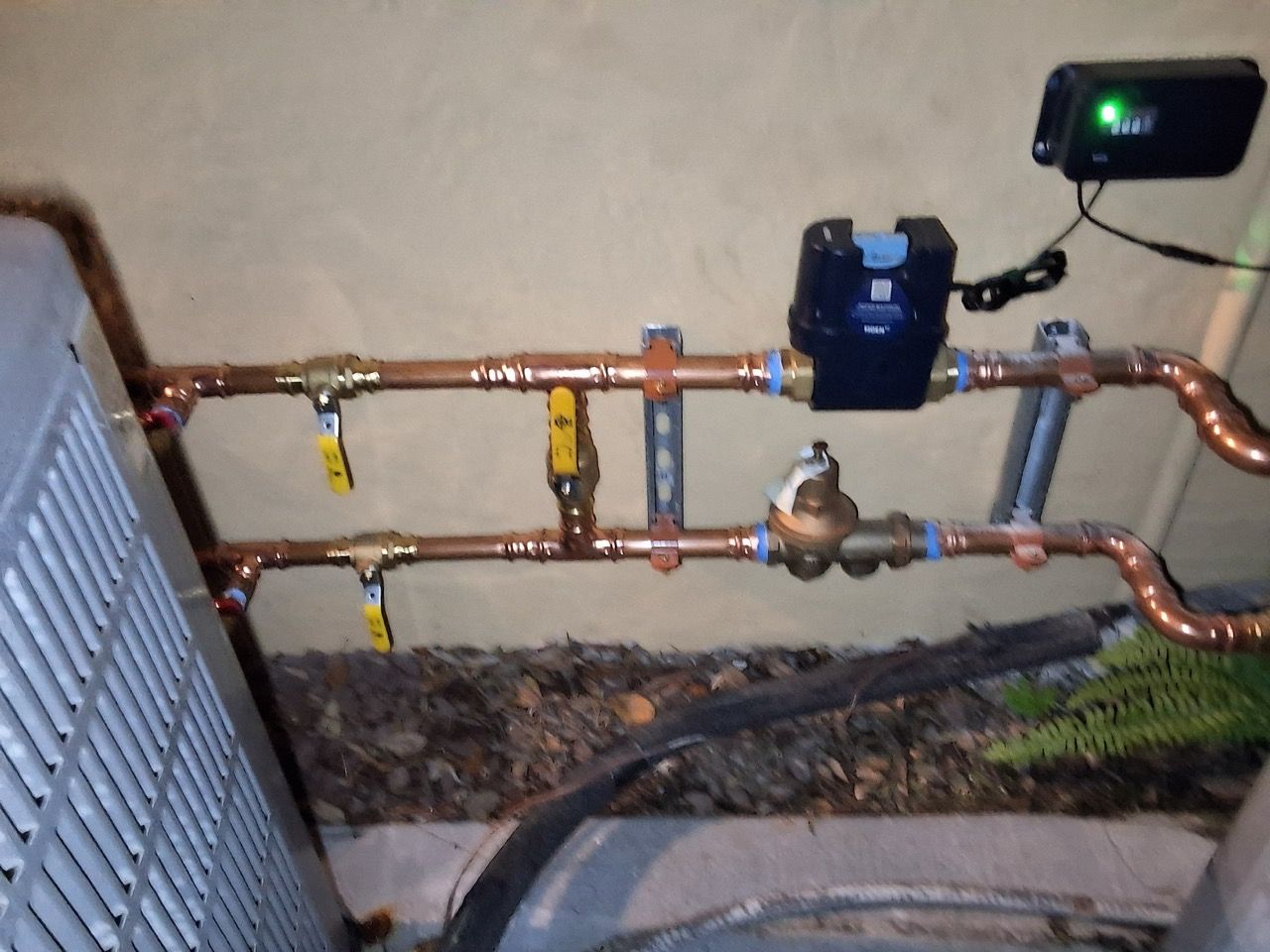 Copper pipes with valves and a meter on a wall, likely a utility or plumbing installation.