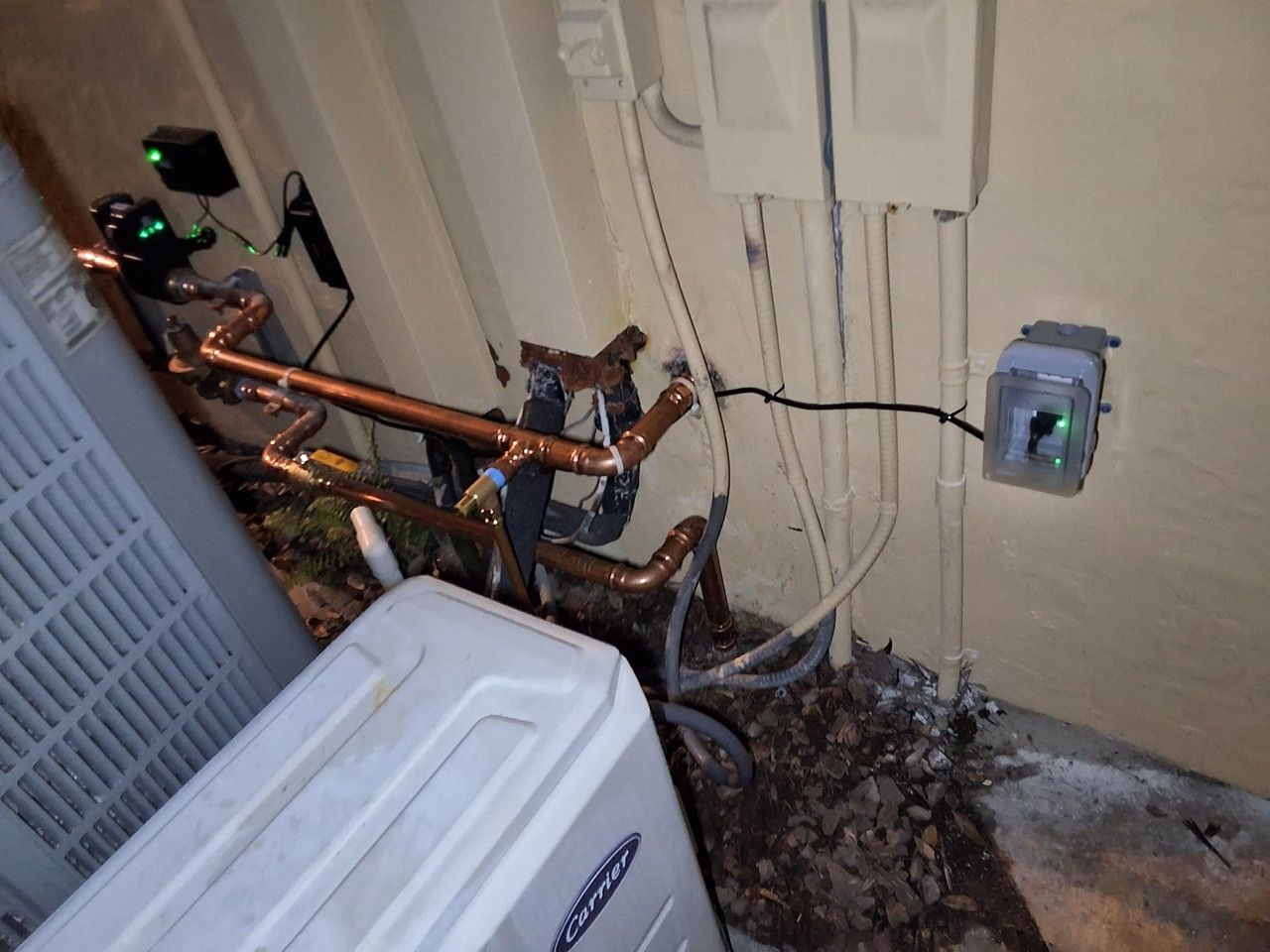 Damaged copper pipes and electrical wires exposed on a basement wall near a utility box
