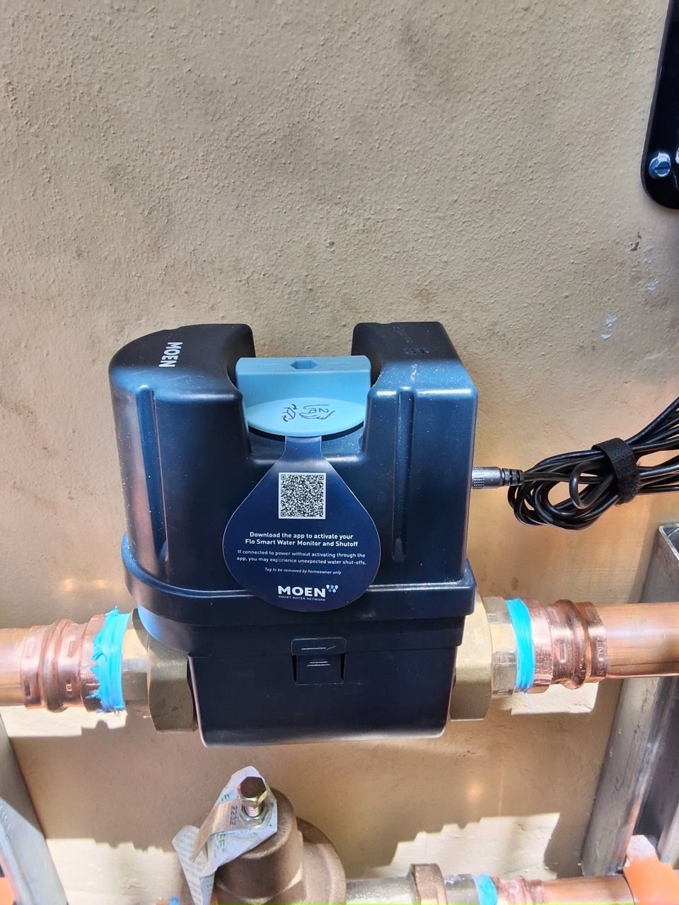 Water meter with digital display and copper pipes mounted on a wall.