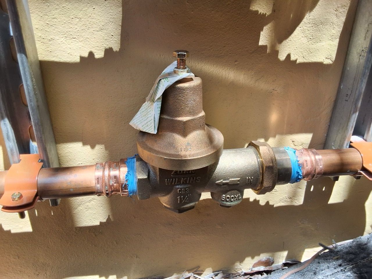 Water pipe assembly with a bronze pressure regulator and copper pipes against a wall.