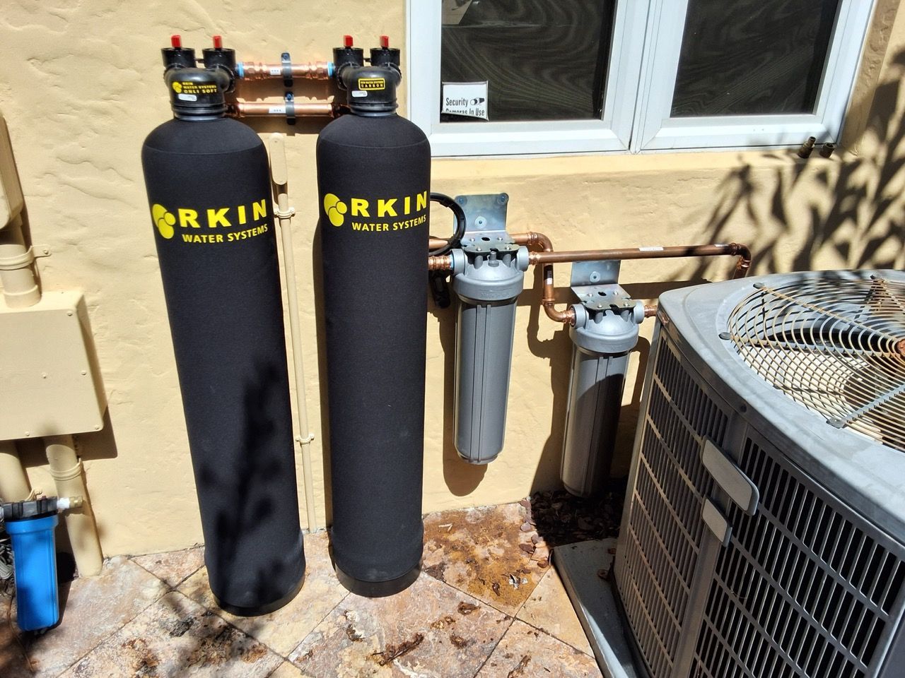 Two black Orkin water filter tanks beside an outdoor AC unit on a concrete patio.
