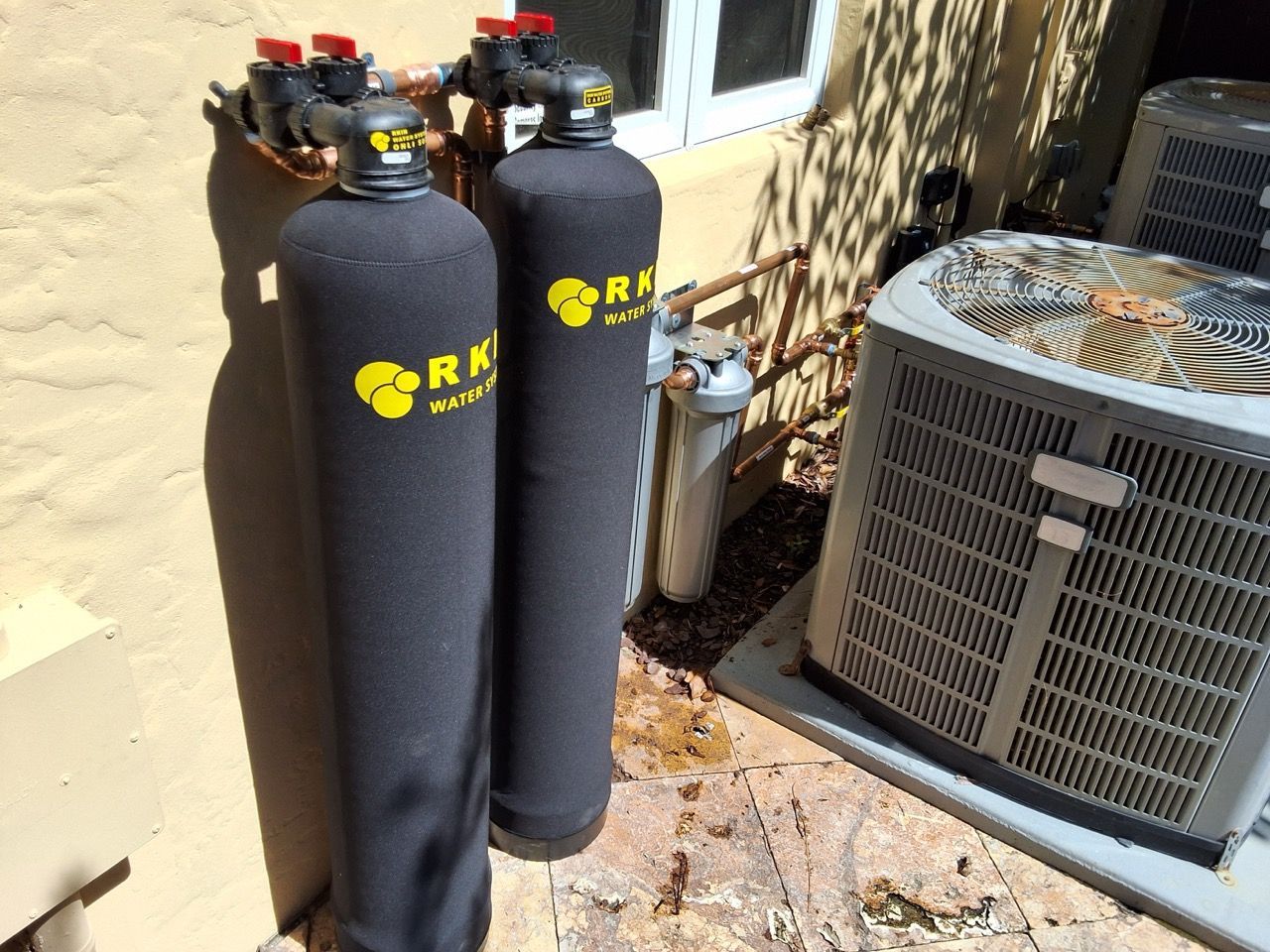 Two black water softener tanks and an outdoor HVAC unit beside a house wall