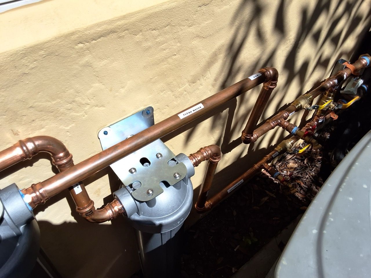 Copper pipes and a meter installed along a beige exterior wall with dry leaves nearby