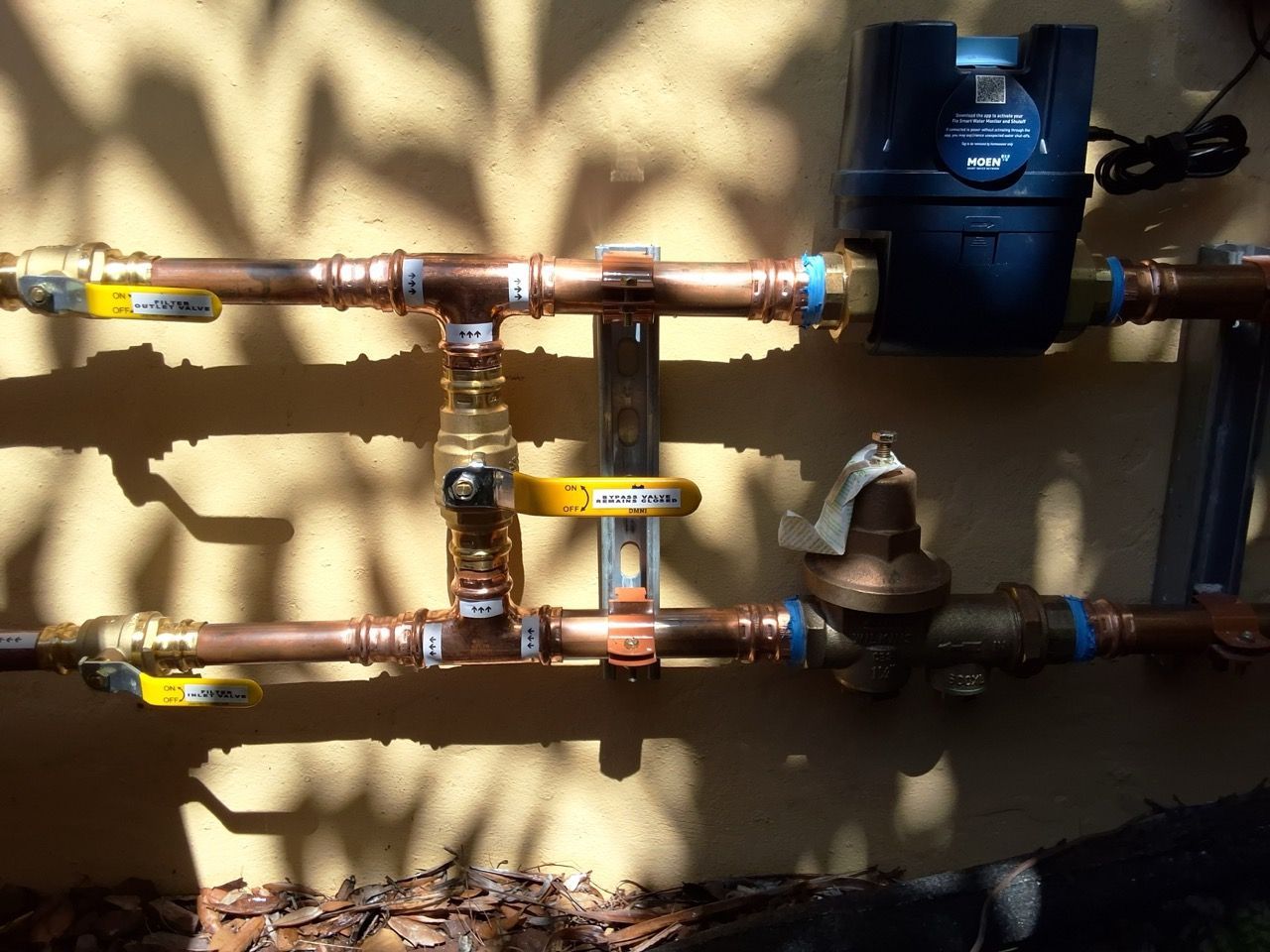 Copper pipes and valves on a wall with a blue water meter and shadows in sunlight