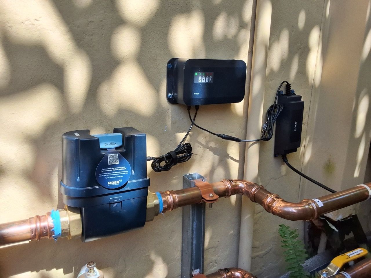 Outdoor utility meters and copper pipes mounted on a beige wall in dappled sunlight