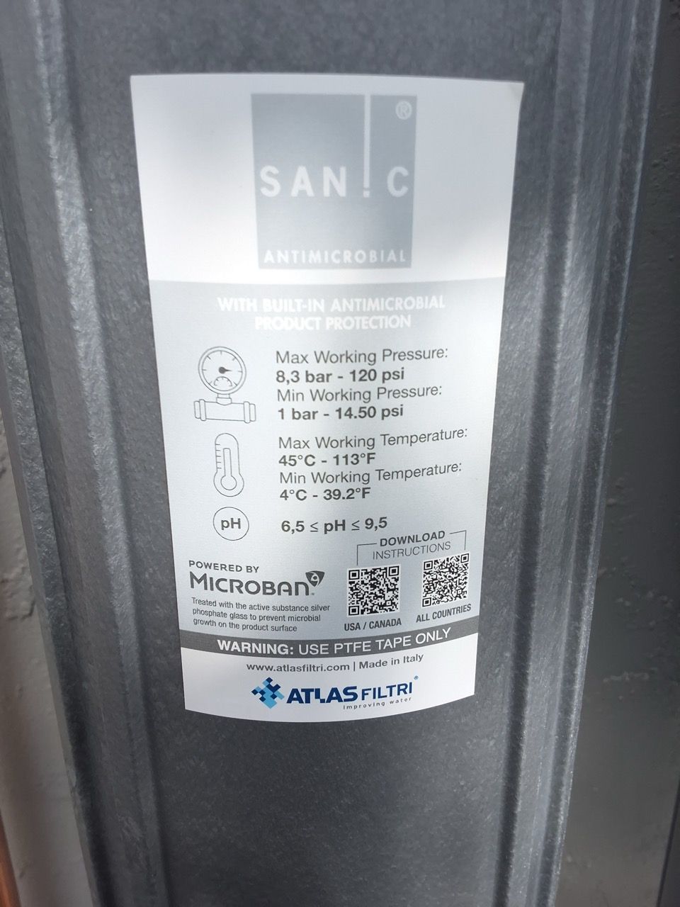 Close-up of a white industrial equipment label with small text and QR codes on a gray metal surface.