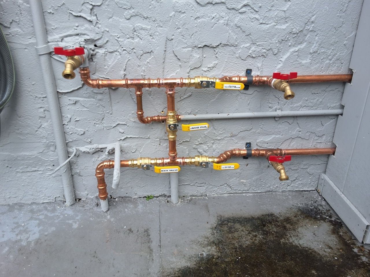 Outdoor copper plumbing pipes with red and yellow shutoff valves on a stucco wall