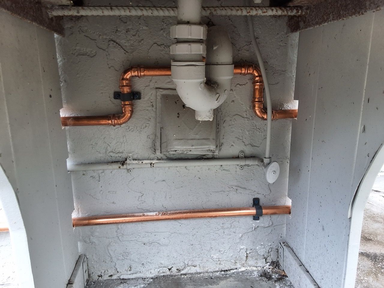 Open utility niche with copper pipes and gray walls, showing exposed plumbing inside a wall cavity
