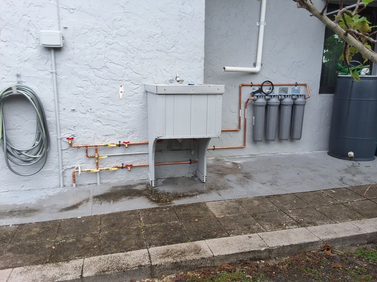 Exterior wall with utility pipes, meter boxes, and cables beside a concrete walkway.