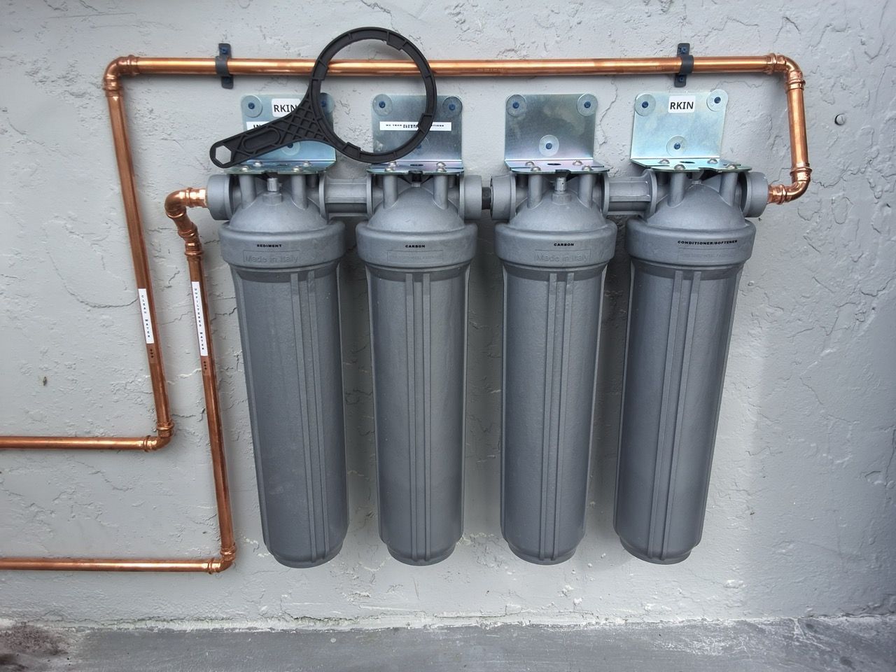 Copper plumbing manifold with four gray water filter canisters mounted on a wall