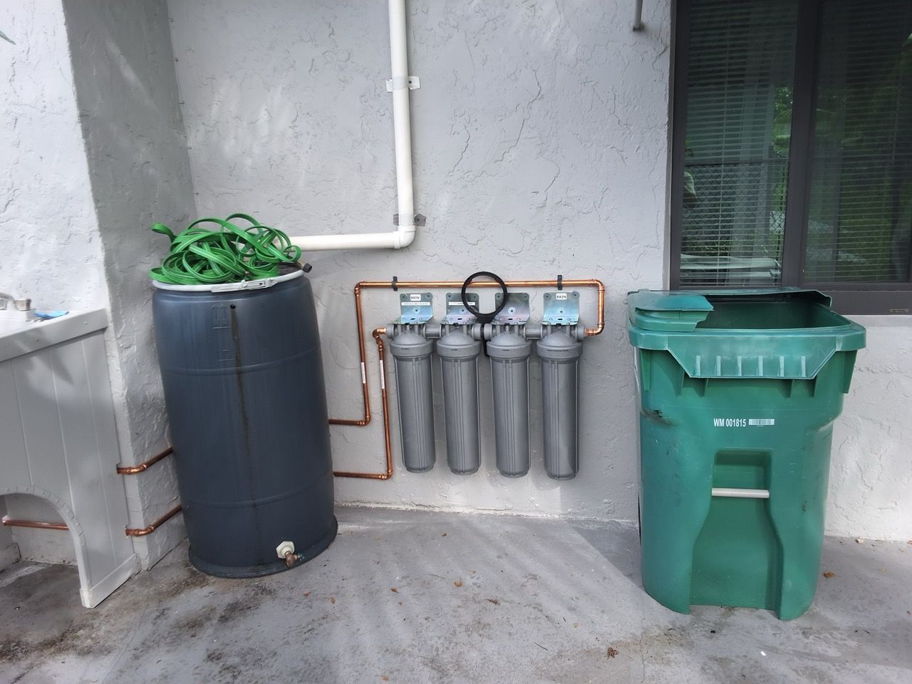 Water filtration setup with three metal cylinders, a blue tank, and a green bin against a wall outside