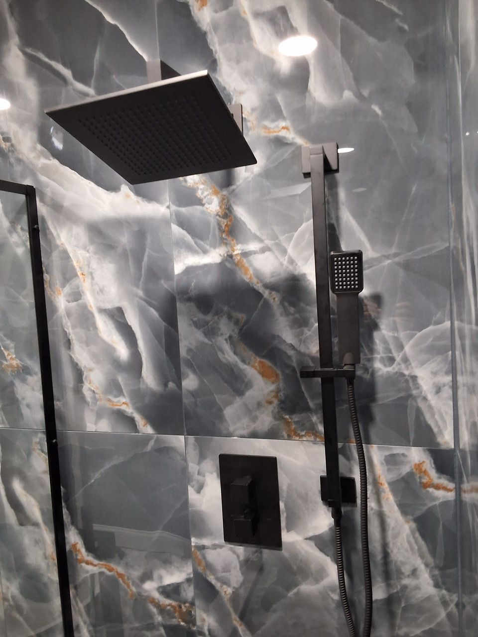 Modern shower with marble-pattern tile, black rainfall head, and handheld spray unit