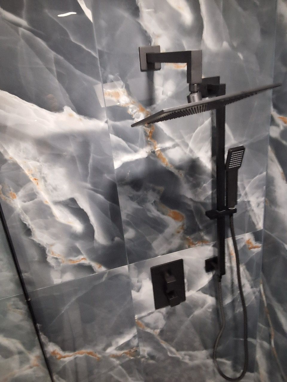 Black shower fixture with handheld sprayer against a gray marble-pattern tile wall